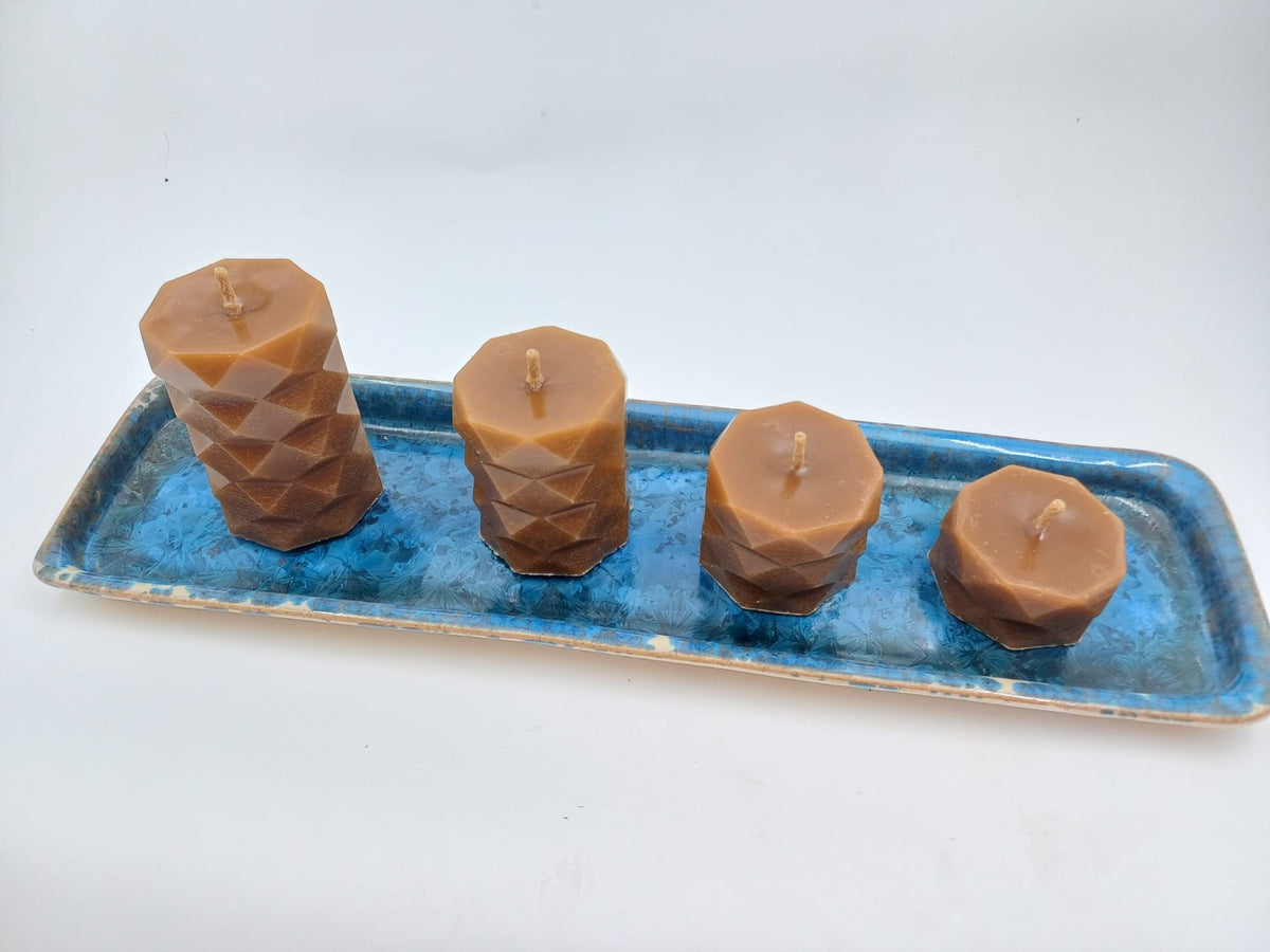 Faceted beeswax pillars in four sizes displayed on a blue ceramic tray